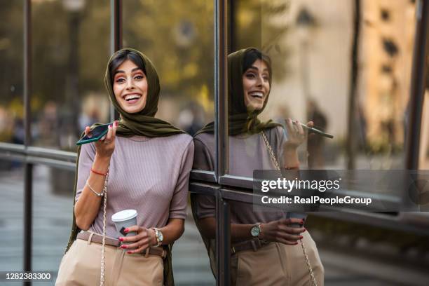 美しいイスラム教徒の女性が電話で話し、路上でコーヒーを飲む - arab woman fashion ストックフォトと画像