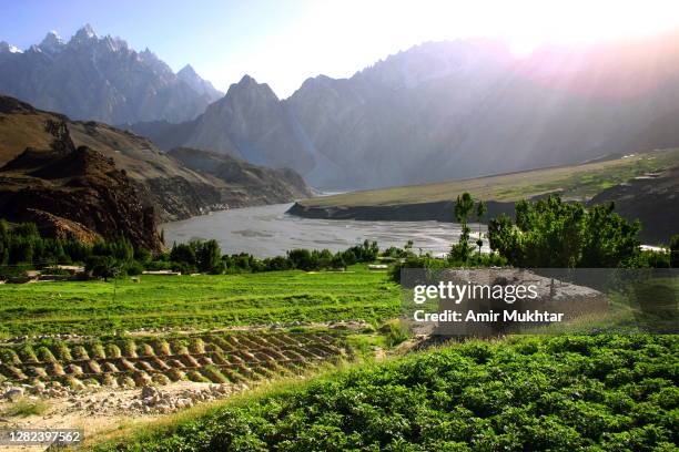 plowed agricultural land in front of river indus and passu cones muntains. - indus river pakistan stock pictures, royalty-free photos & images