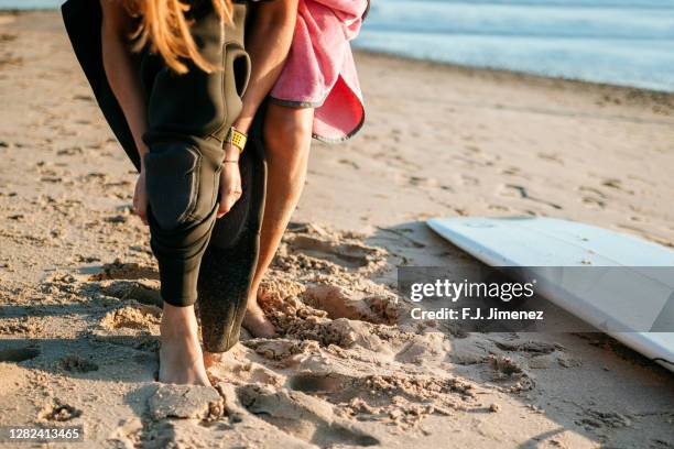 woman straining her wetsuit on the beach - neoprene stock-fotos und bilder