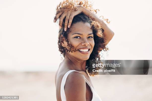 風の強い日にビーチを歩く美しい若い女性 - 髪に手をやる　女性 ス��トックフォトと画像