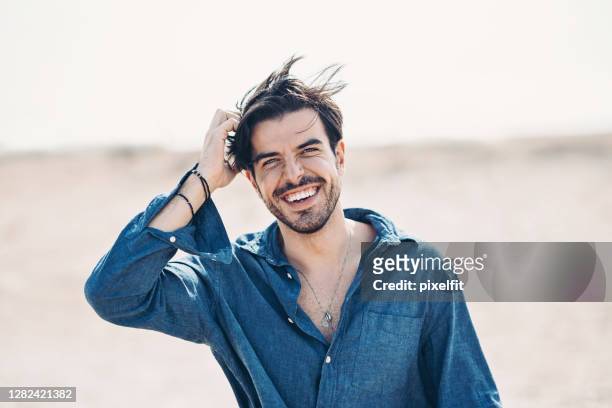 hübscher mann zu fuß am strand an einem windigen tag - tousled hair stock-fotos und bilder