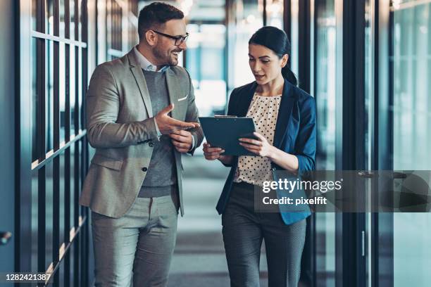 couple of business persons walking in the corridor and talking - man with clipboard imagens e fotografias de stock