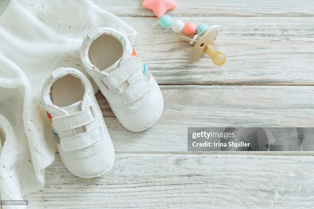 Baby white shoes and warm blanket on wooden background.