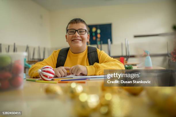 school boy smiling while seating at the desk in the classroom - last day of school stock pictures, royalty-free photos & images