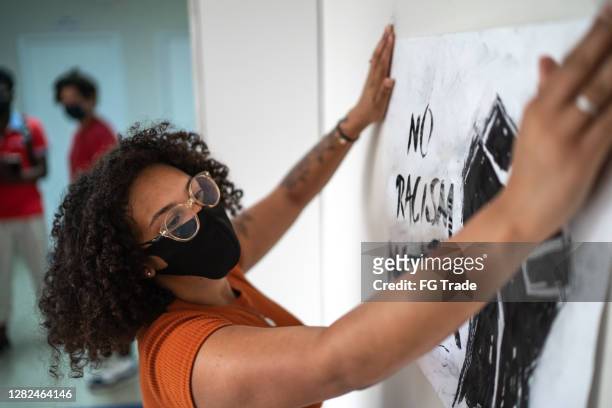 estudiante mujer usando máscara de la cara poniendo cartel en la pared de la escuela - blm fotografías e imágenes de stock