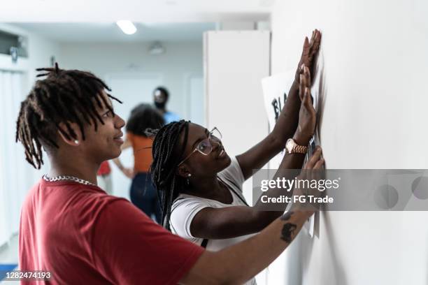 students fixing a anti-racist poster in the wall - students union stock pictures, royalty-free photos & images