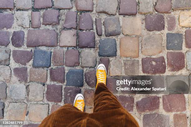 man in canvas shoes walking on cobbled street, directly above personal perspective view - looking above stockfoto's en -beelden