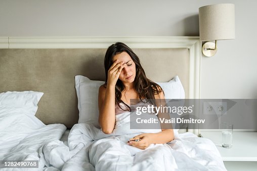 Young caucasian woman lying in bed, feeling unwell, with her hand on her head. Sickness / illness concept. Coronavirus / fever / headache concept. Home isolation. Young caucasian woman lying in bed, feeling unwell, with her hand on her head. Sickness / illness concept. Coronavirus / fever / headache concept. Home isolation.