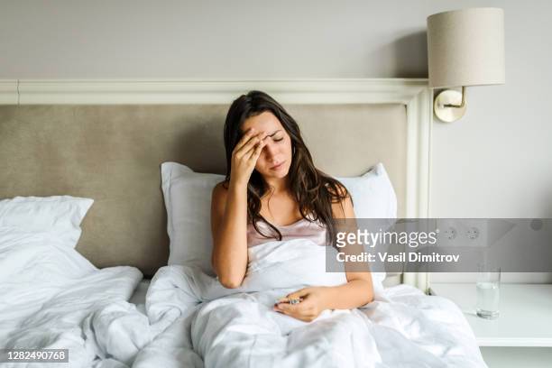 young caucasian woman lying in bed, feeling unwell, with her hand on her head. sickness / illness concept. coronavirus / fever / headache concept. home isolation. - symptom stock pictures, royalty-free photos & images