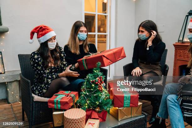 vrienden die giften voor kerstmis ruilen die gezichtsmaskers dragen - four people stockfoto's en -beelden