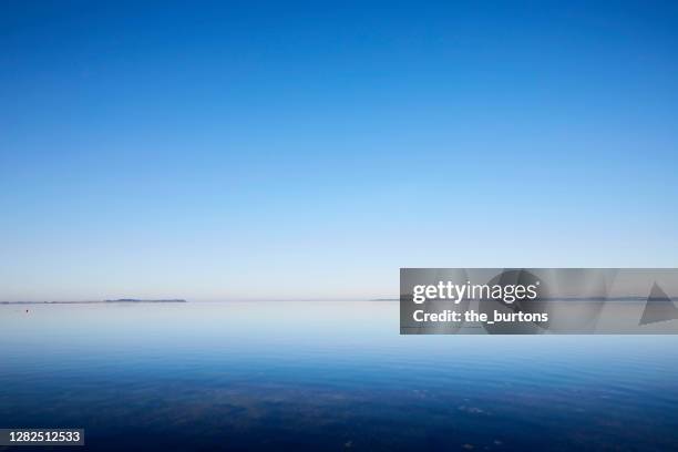 smooth water surface at the sea and reflection of fog and blue sky during sunrise in the morning - 空気感 ストックフォトと画像