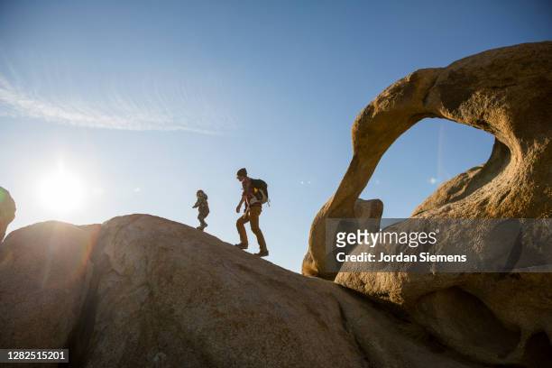 a young boy and his father hiking a rocky trail in the mountains with an arch in the scene. - lone pine california fotografías e imágenes de stock
