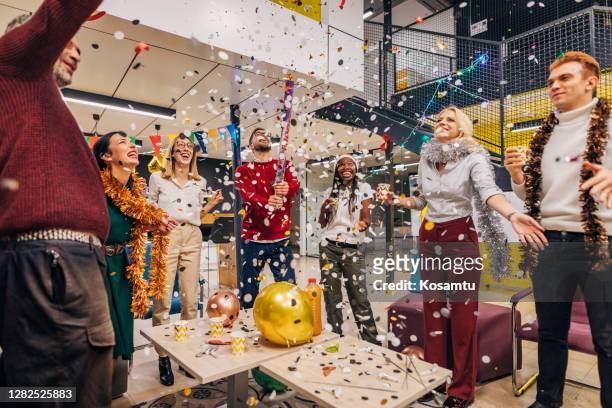 after hard working year cheerful diverse group of entrepreneurs celebrating new year's eve at their modern office - office party imagens e fotografias de stock