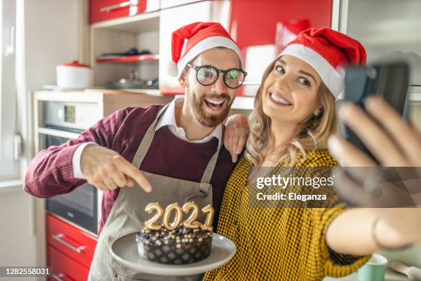 coppia innamorata che si fa un selfie con la torta al cioccolato, si diverte e festeggia il capodanno a casa; coppia con videochiamata con gli amici per capodanno - christmas cake foto e immagini stock