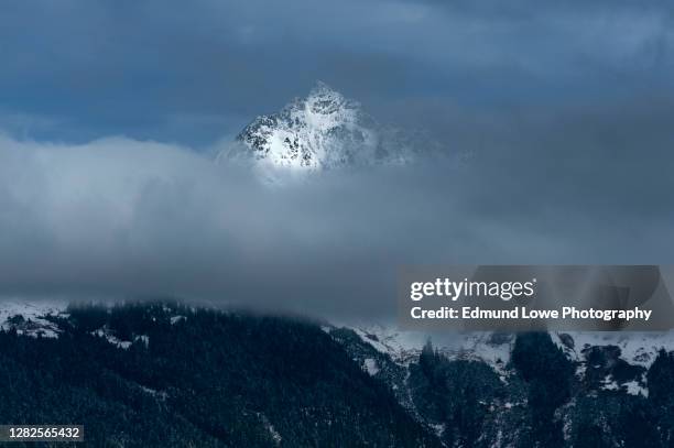 dramatic light on a snow capped mountain peak in the north cascades. - ominous mountains stock pictures, royalty-free photos & images