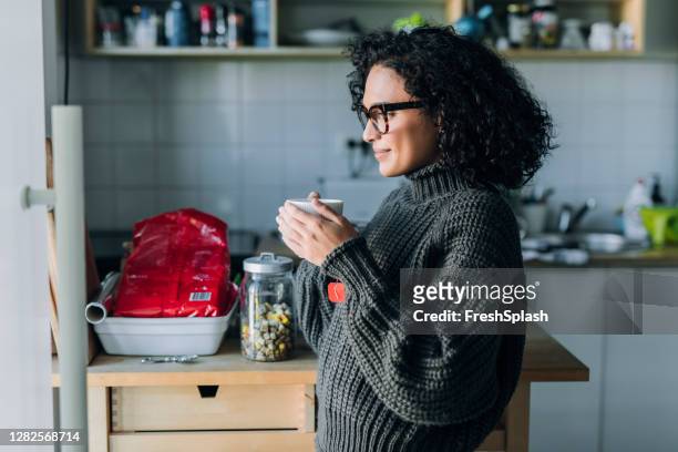 gesunde morgengewohnheiten: eine junge mixed race frau, die heißen tee in der küche trinkt - feierliche veranstaltung stock-fotos und bilder