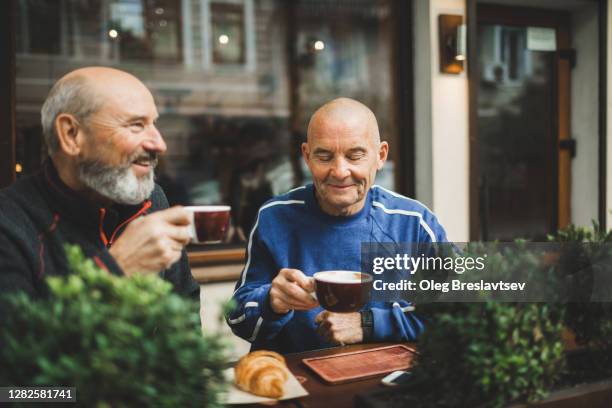 two old age senior friends drinking coffee in cafe on outside terrace. laughing and talking. young at heart - man in bar stockfoto's en -beelden