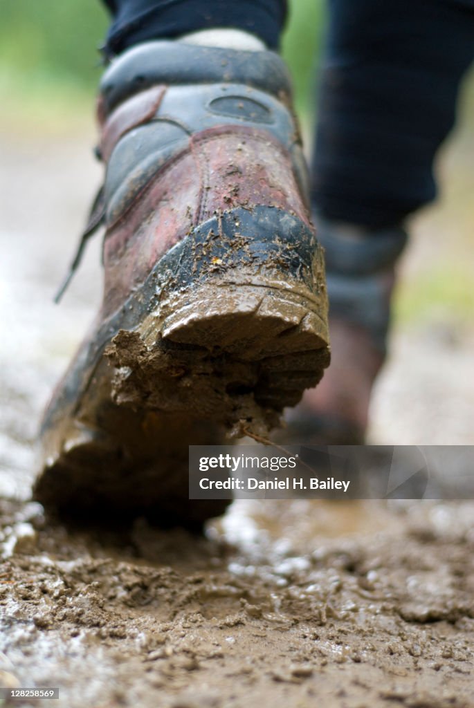 Close-up of hiking boots walking on a trail through the mud