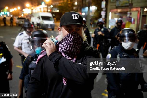 Man holds on to his mobile phone as police officers stand guard outside the 4th District Police Station during a protest against the death of Karon...