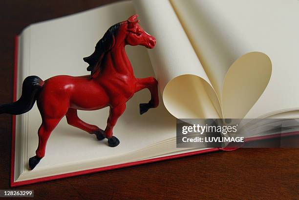 red toy horse stepping on a book - eversofine stock pictures, royalty-free photos & images