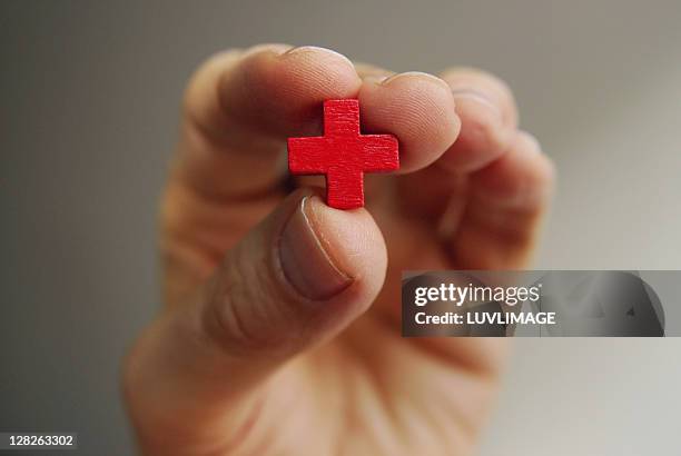 male fingers hold a little red cross - red cross foto e immagini stock