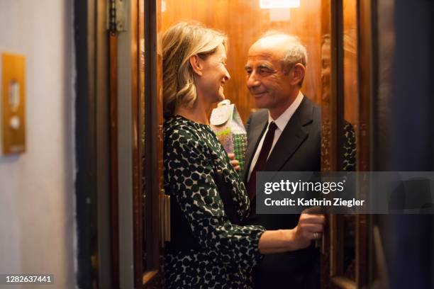 mature couple in an elevator, man holding a present - elevator doors stock pictures, royalty-free photos & images