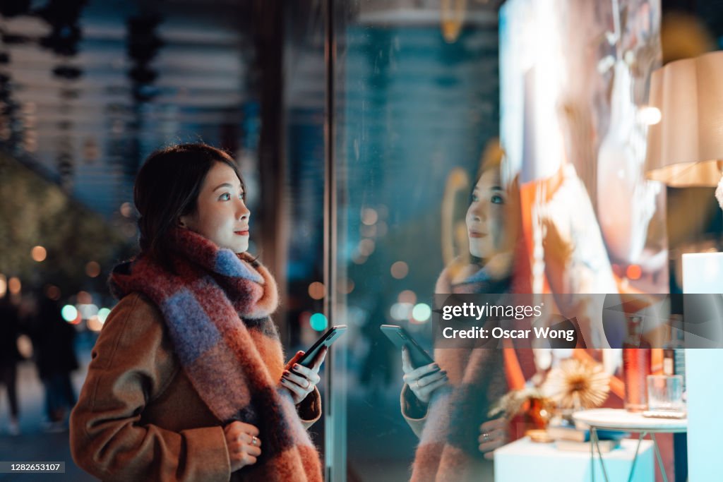 Young woman window shopping in the city at night