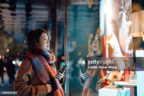 young woman window shopping in the city at night - buying stock-fotos und bilder