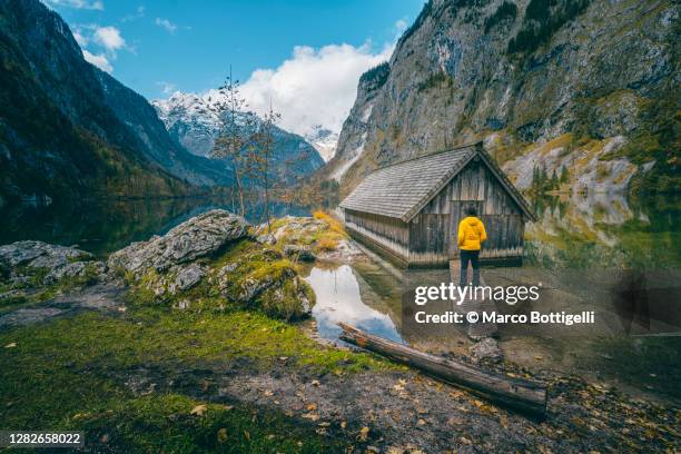 man looking at view at lake konigssee next to boathouse, bavaria, germany - wooden hut stock pictures, royalty-free photos & images