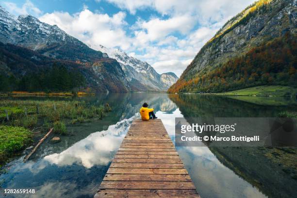 one man sitting on a boat pier admiring the konigssee lake, bavaria, germany - journey stock-fotos und bilder