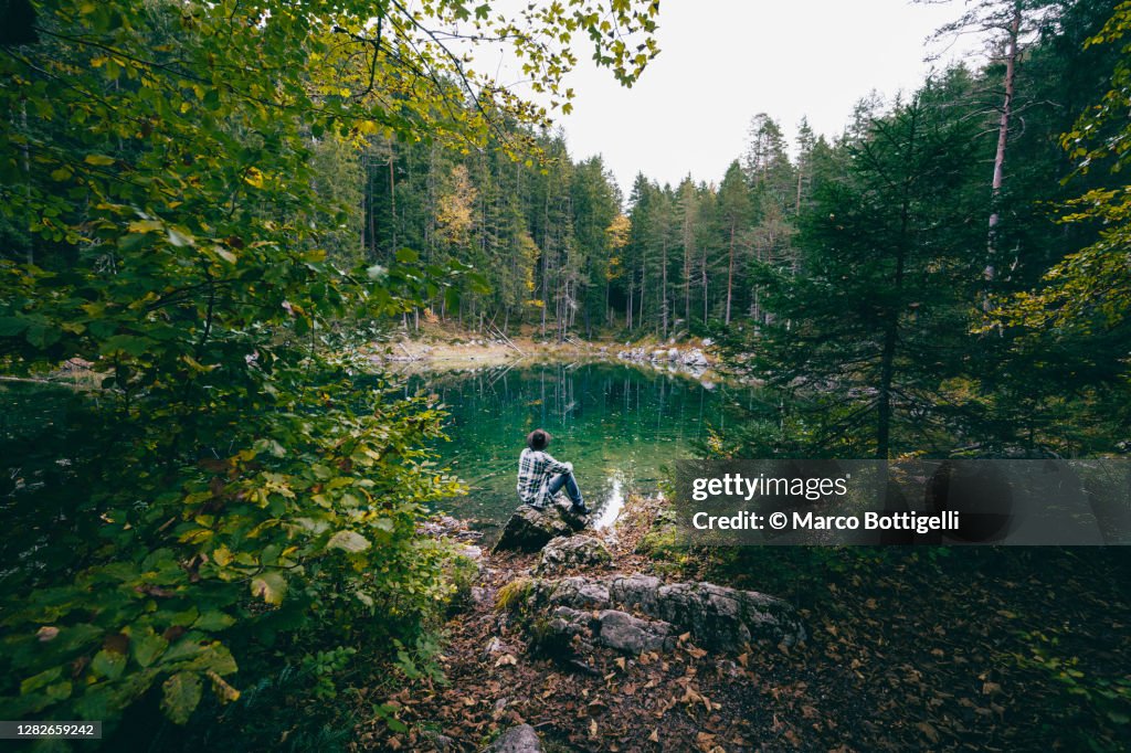 Man sitting admiring an emerald lake in the forest