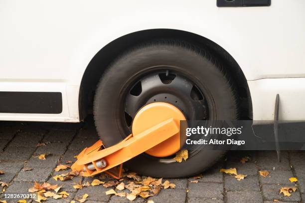 white vehicle wheel with a orange clamp to immobilize it. berlin. germany. - parkkralle stock-fotos und bilder