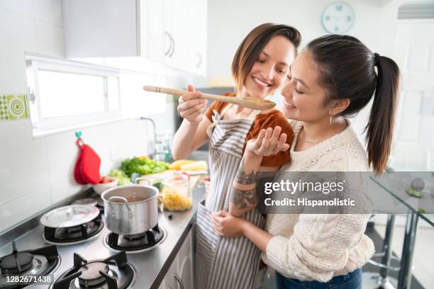 gay couple cooking at home and feeding each other while smiling - gay couple cooking stock pictures, royalty-free photos & images