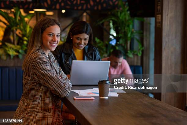 the businesswoman looks at the camera in a portrait while sitting at the bar and in the background his coworkers see - law student stock pictures, royalty-free photos & images