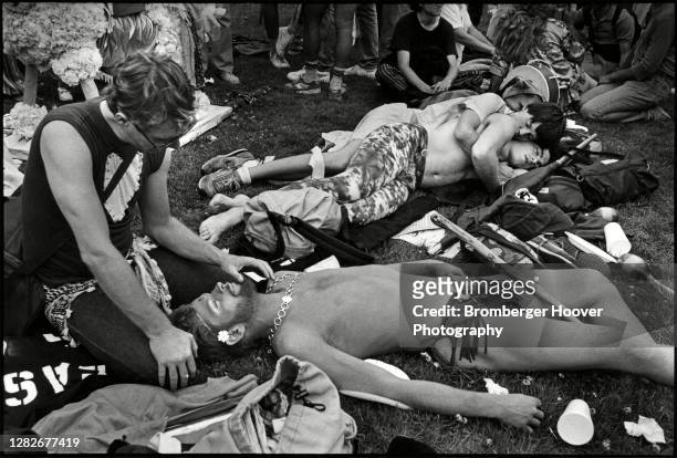 View of a man sunbathing in a loincloth as another man strokes his beard, on the grass outside the Civic Center during the International Lesbian &...