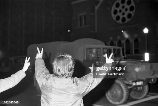 An anti-war protestor gives "Peace" signs as a convoy of National Guard Jeeps roll out to patrol Washington streets after police and protestors...