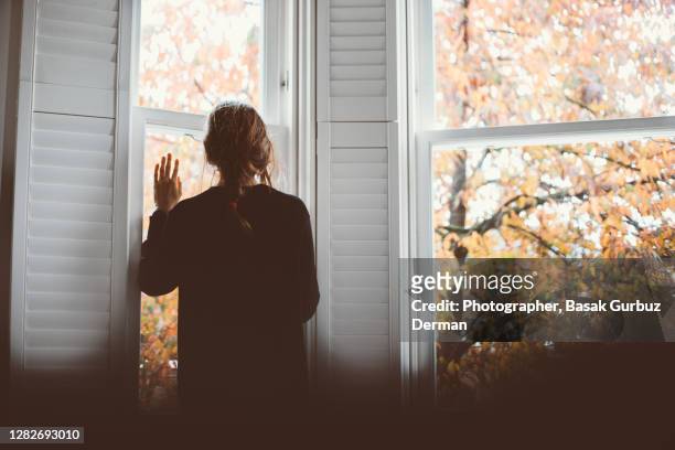 a woman looking through the window... social distancing. - depression sadness stock pictures, royalty-free photos & images