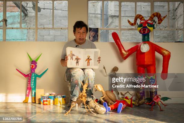 David Linares poses for a portrait showing the book entitled "En Calavera" as well as his craftworks of devils and alebrijes, during a day of work at...