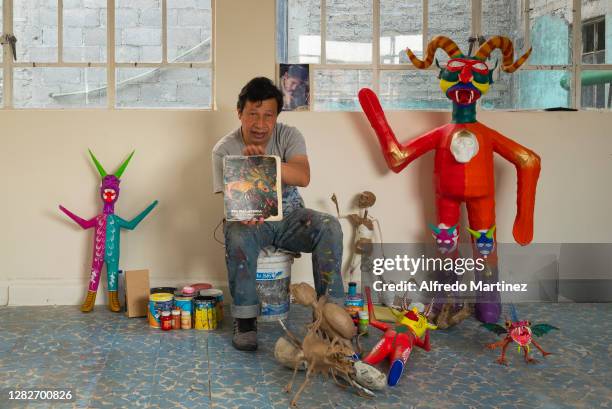 David Linares poses for a portrait showing the book entitled "En Calavera" as well as his handicrafts of devils and alebrijes during a day of work at...