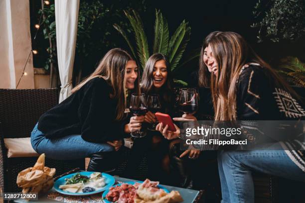friends drinking red wine and looking at a smartphone together - patio restaurant stock pictures, royalty-free photos & images