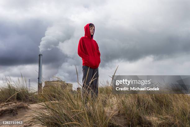 teenage boy stands looking ahead with power plant fumes behind him - climate change kids stock pictures, royalty-free photos & images