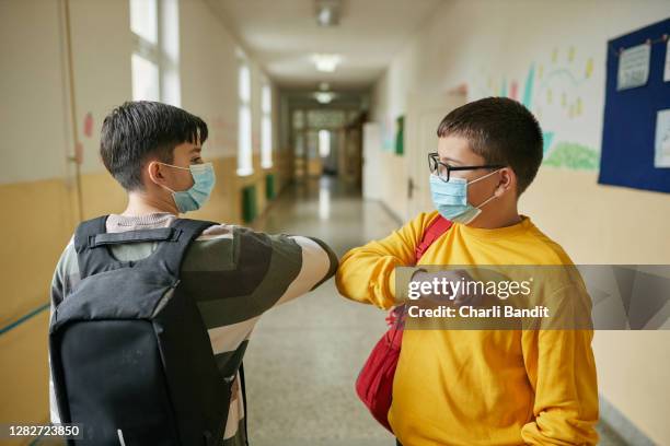 responsible elementary student using a elbow bump as a alternative handshake during covid-19 pandemic - social distancing school stock pictures, royalty-free photos & images