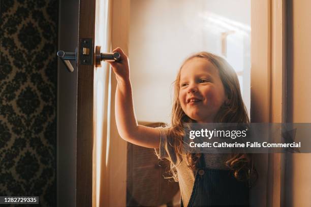 happy little girl opens an interior door and peeks around into a dark room - knocking photos et images de collection