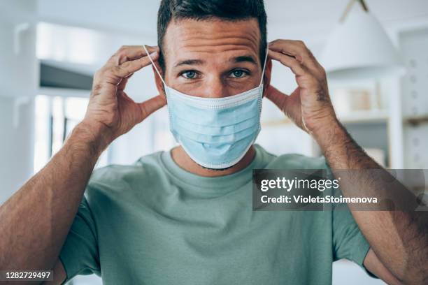 young man putting protective medical face mask. - surgical mask man stock pictures, royalty-free photos & images