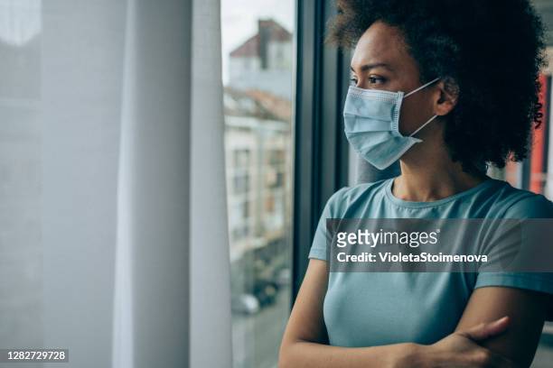 worried young woman looking through window at home in quarantine. - quarantine stock pictures, royalty-free photos & images