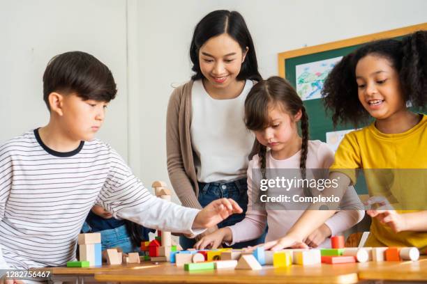 lehrer beobachtet multiethnische kinder spielen mit holzblöcken im klassenzimmer - lehrtätigkeit stock-fotos und bilder