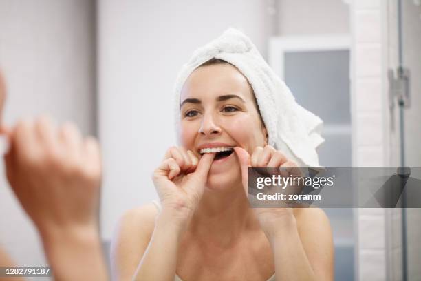 réflexion de femme avec la serviette sur la tête nettoyant ses dents avec la soie dentaire - gencive photos et images de collection