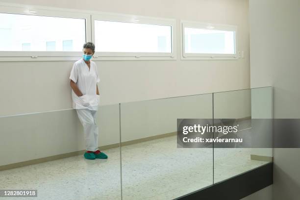 mature nurse standing in hospital corridor taking a break - shoe covers stock pictures, royalty-free photos & images