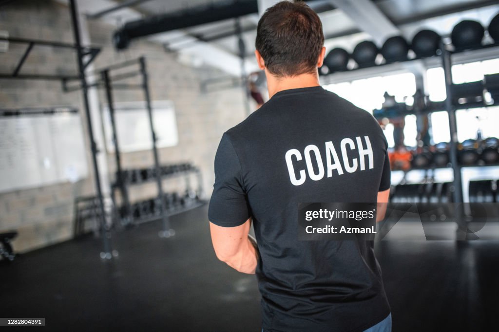 Adatta allenatore maschile caucasico in piedi nella palestra di allenamento incrociato