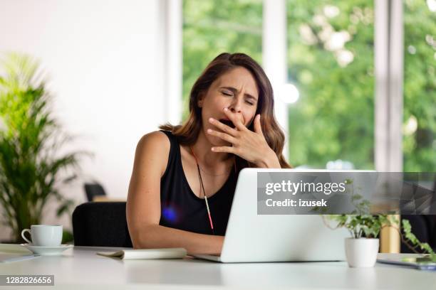 vermoeide jonge vrouw die aan computer in het groene bureau werkt - yawning woman stockfoto's en -beelden